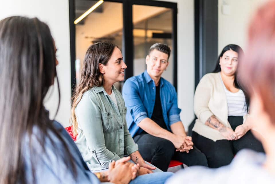 Group of people sitting in circle listening to one person speak.